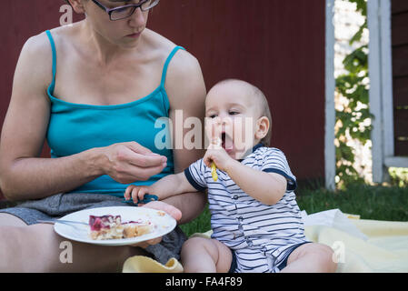 Baby Boy essen Kuchen vom Teller seiner Mutter in Rasen, München, Bayern, Deutschland Stockfoto