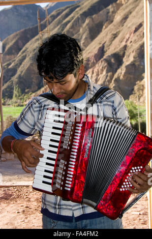 Sonnendurchflutetes junger Mann im gestreiften Hemd Das Handorgelspiel Bergkulisse in Bolivien, Südamerika. Stockfoto