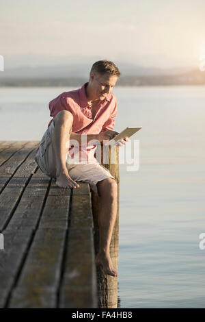 Reifer Mann mit digital-Tablette am Pier von See, Bayern, Deutschland Stockfoto