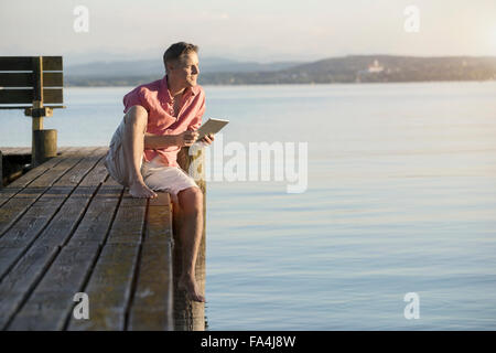 Reifer Mann mit digital-Tablette auf Pier und mit Blick auf See, Bayern, Deutschland Stockfoto