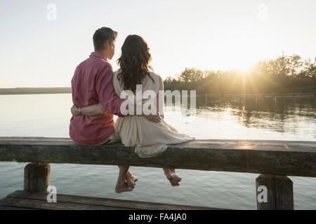 Älteres Paar sitzt am Pier Blick auf Sonnenuntergang, Bayern, Deutschland Stockfoto