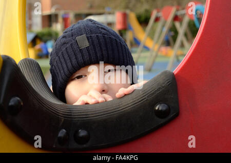 Ein kleiner Junge schaut durch ein Fenster in einem Klettergerüst auf einem Spielplatz. Stockfoto