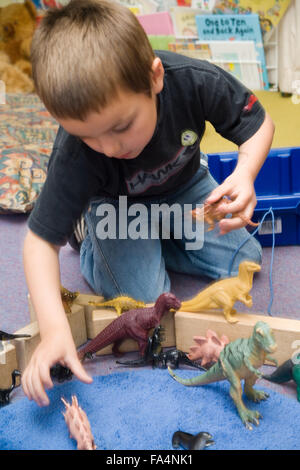 Junge kniend am Boden im Unterricht spielen mit Spielzeug Dinosaurier, Stockfoto