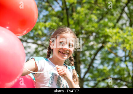 Porträt eines lächelnden Mädchens halten rote Luftballons, München, Bayern, Deutschland Stockfoto