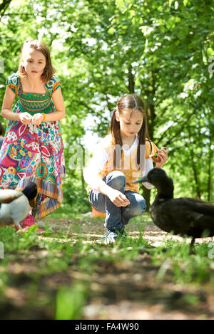 Zwei Mädchen, die Verfütterung von Brezel an Enten im Park, München, Bayern, Deutschland Stockfoto