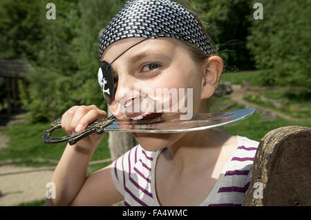 Porträt eines Mädchens verkleidet als Pirat beißen Säbel auf Spielplatz, Bayern, Deutschland Stockfoto