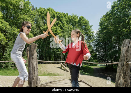 Zwei Mädchen, so zu tun als Piraten kämpfen mit Schwertern in Abenteuer Spielplatz, Bayern, Deutschland Stockfoto