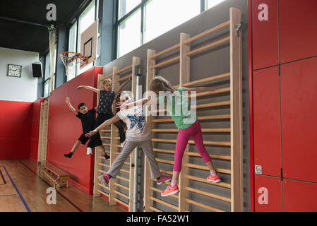 Vier Kinder trainieren auf Sprossenwand in Sporthalle, München, Bayern, Deutschland Stockfoto