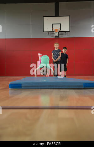 Mädchen tun Purzelbaum auf Gymnastikmatte in Sporthalle mit ihren Freunden, München, Bayern, Deutschland Stockfoto