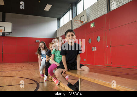 Kinder auf Bank vor Übungen in großen Turnhalle der Schule, Bayern, München, Deutschland Stockfoto