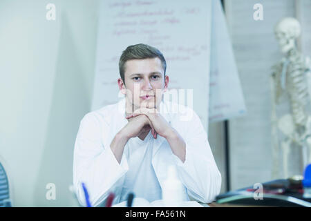 Porträt eines jungen Arztes, sitzt in seinem Büro und Skelett im Hintergrund, Baden-Württemberg, Deutschland Stockfoto