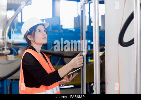 Ingenieurin mithilfe einer digitalen-Tablets und durch Überprüfung der Maschine in einer Industrieanlage, Baden-Württemberg, Deutschland Stockfoto