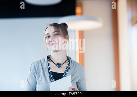 Reife Frau mit Zwischenablage lächelnd in Hörsaal, Freiburg Im Breisgau, Baden-Württemberg, Deutschland Stockfoto