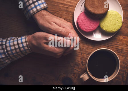 Kaffee und Macaron Cookies am Morgen, männlichen Händen halten Tasse mit Heißgetränk, Draufsicht, Retro-getönt Stockfoto