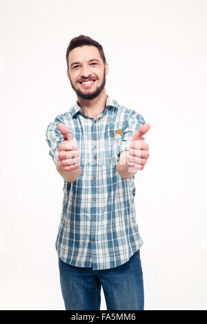 Lächelnd attraktiven jungen Mann mit Bart im karierten Hemd und Jeans auftauchen Daumen mit beiden Händen auf weißem Hintergrund Stockfoto