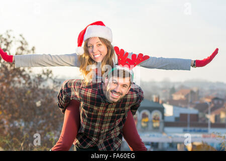 Paar in Liebe Huckepack Reiten im Freien mit Weihnachtsmützen Stockfoto