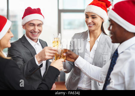 Glückliche Kollegen in Santa Kappen Toasten mit Champagner am Firmenfeier Stockfoto