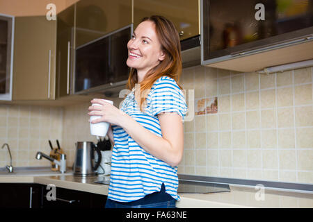 Lächelnde fröhliche junge Frau in gestreiften T-shirt, lachen und trinken Tee in Küche Stockfoto