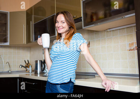 Glücklich fröhlich niedliche junge schwangere Frau stehend auf Küche und Tee trinken Stockfoto