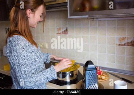 Schönes Lächeln auf den Lippen rothaarige junge Frau in graue Strickpullover Pastaherstellung in Küche Stockfoto