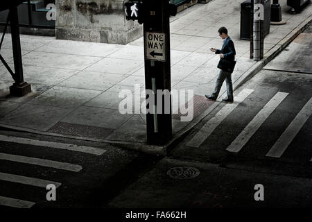 Ein Mann zu Fuß auf einer Straßenkreuzung, Blick auf ein Telefon in der Hand. Stockfoto