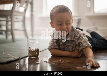 Ein Kind, liegend auf dem Bauch auf dem Boden spielen mit Münzen und setzen sie in ein Glas. Stockfoto