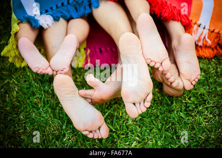 Vier Paar Füsse durchhalten Ende eine bunte Decke auf dem Rasen Stockfoto