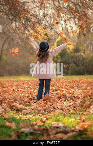 Rückansicht eines Mädchens werfen Herbst Blätter in der Luft Stockfoto