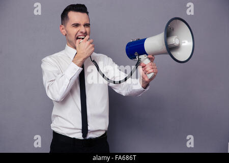 Porträt eines jungen Geschäftsmann schreiend in Megaphon auf grauem Hintergrund Stockfoto