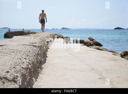 Rückansicht des Mannes zu Fuß entlang der Wand von Strand, Ibiza, Spanien Stockfoto