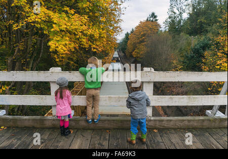 Drei Kinder auf Brücke beobachten Zug fahren unter Stockfoto