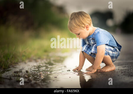 Junge spielt in einer Pfütze Wasser Stockfoto