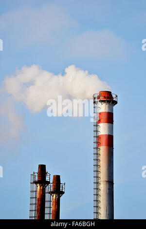 Rauch und Dampf, die sich aus einem petrochemischen Industrieanlagen Schornstein mit einem blauen Himmel im Hintergrund Stockfoto