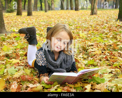 junges Mädchen liest ein Buch im Herbst Park auf dem Boden liegend Stockfoto