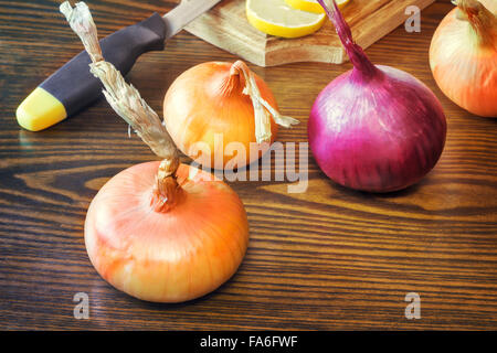 Auf dem Tisch liegt eine große Zwiebel, Zitrone auf einem Brett und einem Küchenmesser. Stockfoto