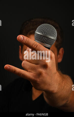 Männliche Hand Mikrofon mit Teufelshörnern Rock Metal mit Namensschild Kopf hinter isoliert auf schwarzem Hintergrund Stockfoto