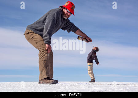 Optische Täuschung, Man gießt Bier in kleinen Mannes Mund, Salar de Uyuni, Bolivien Mund Stockfoto