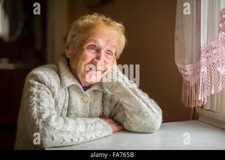 Glückliche ältere Frau sitzt an einem Tisch am Fenster. Stockfoto