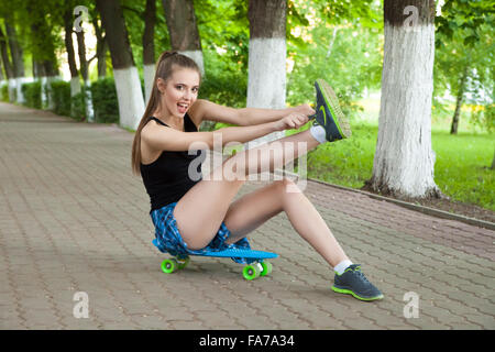 Schöne junge Frau sitzend über skateboard Stockfoto