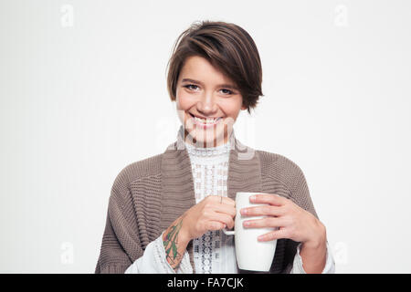 Fröhlich hübsche junge Frau in Strickjacke halten weiße Tasse und trinken auf weißem Hintergrund Stockfoto