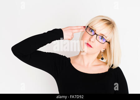 Eine junge schlanke blonde blonde behaarte Frau Mädchen, UK, mit Brille, schießen sich in den Kopf mit den Fingern in Form einer gefälschten Pistole Stockfoto