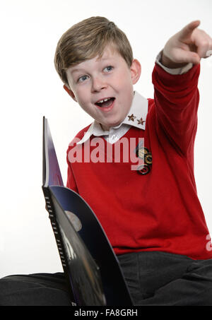 Ein Junge (Grundschulalter) junge in einem roten Schule einheitliche Pullover Bücher zu lesen und Schreiben von Notizen für seine Hausaufgaben. Stockfoto