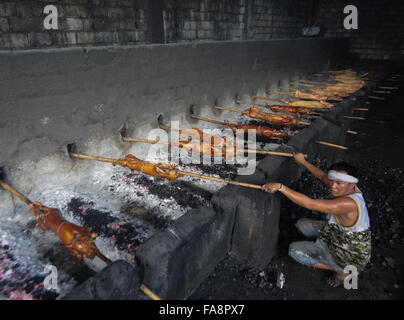 Quezon City, Philippinen. 23. Dezember 2015. Ein Filipino Worker übernimmt gebratenes Schwein gekocht in Bambus Rotiserries bei Vorort Quezon City, östlich von Manila, Philippinen. Gebratenes Schwein, genannt "Lechong Baboy" oder einfach "Lechon" ist eine beliebte Delikatesse während der Weihnachtszeit in den Philippinen. Das Land feiert die längste Weihnachtszeit in der Welt, die bereits im September beginnt. © Richard James M. Mendoza/Pacific Presse/Alamy Live-Nachrichten Stockfoto