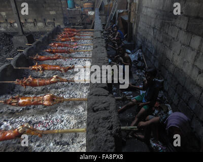 Quezon City, Philippinen. 23. Dezember 2015. Philippinische Arbeiter behandeln gebratene Schweine gekocht in Bambus Rotiserries bei Vorort Quezon City, östlich von Manila, Philippinen. Gebratenes Schwein, genannt "Lechong Baboy" oder einfach "Lechon" ist eine beliebte Delikatesse während der Weihnachtszeit in den Philippinen. Das Land feiert die längste Weihnachtszeit in der Welt, die bereits im September beginnt. © Paola Visone/Pacific Press/Alamy Live-Nachrichten Stockfoto