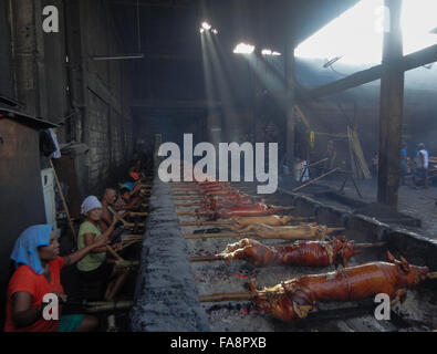 Quezon City, Philippinen. 23. Dezember 2015. Philippinische Arbeiter behandeln gebratenes Schwein gekocht in Bambus Rotiserries bei Vorort Quezon City, östlich von Manila, Philippinen. Gebratenes Schwein, genannt "Lechong Baboy" oder einfach "Lechon" ist eine beliebte Delikatesse während der Weihnachtszeit in den Philippinen. Das Land feiert die längste Weihnachtszeit in der Welt, die bereits im September beginnt. © Richard James M. Mendoza/Pacific Presse/Alamy Live-Nachrichten Stockfoto