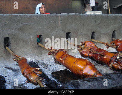 Quezon City, Philippinen. 23. Dezember 2015. Ein Filipino Worker schaut zu, wie ganze Schweine in Bambus ROTISSERIEN im Vorort Quezon City, östlich von Manila, Philippinen geröstet werden. Gebratenes Schwein, genannt "Lechong Baboy" oder einfach "Lechon" ist eine beliebte Delikatesse während der Weihnachtszeit in den Philippinen. Das Land feiert die längste Weihnachtszeit in der Welt, die bereits im September beginnt. © Richard James M. Mendoza/Pacific Presse/Alamy Live-Nachrichten Stockfoto