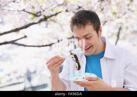 Kaukasischen Mann Essen Sushi mit Stäbchen Hanami in der Saison Stockfoto