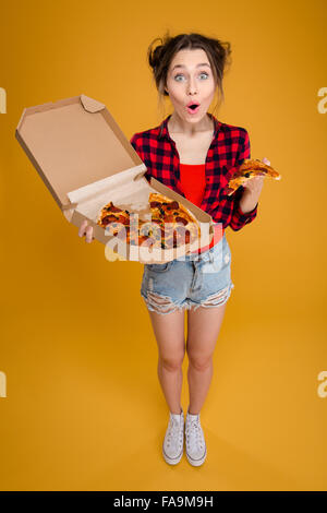 Überrascht gerne hübsche junge Frau im karierten Hemd stehen und wenn Sie mit Pizza auf gelbem Hintergrund Stockfoto