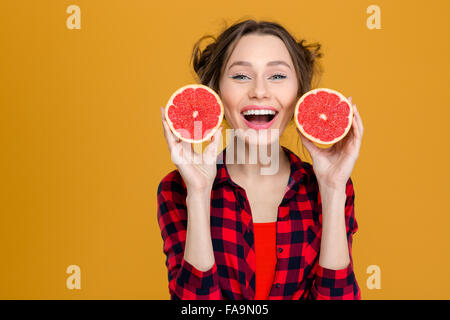Porträt von lächelnden schönen jungen Frau im karierten Hemd mit zwei Hälften der Grapefruit über gelbem Hintergrund Stockfoto