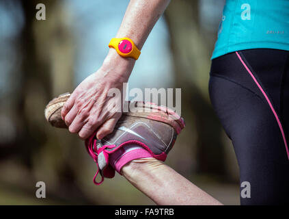 Eine weibliche Jogger tragen ein Aktivitätsprotokoll dehnen vor dem laufen UK Stockfoto